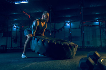 Young healthy man athlete doing exercise exercises with a tire in the gym. Single male model training and practicing hard. Concept of healthy lifestyle, sport, fitness, bodybuilding, crossfit.