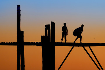 Unidentified people walk on U Bein bridge at sunset in Myanmar.