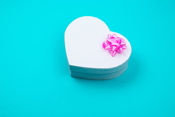 White heart shaped gift box with pink bow for holiday, christmas, thanks giving day, birthday top view isolated on blue background. 