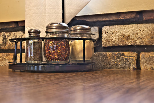 Condiments for pizza. Salt, black pepper, origano, cayenne pepper and paresan cheese on table in restaurant.