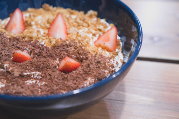 Porridge - healthy breakfast for children and adults. Breakfast cereal with strawberries and chocolate for breakfast in a blue cup on a dark brown wooden table
