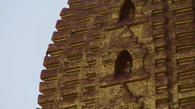 An extreme close up shot of a faded golden painting on a stupa with sculptural designs in Burma
