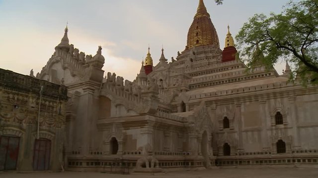 A low angle shot of a big white temple with golden stupas at top of the building in Burma