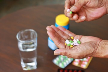 Elderly Asian man holding many pills(tablet and capsule) in hands and pick some medicines for...