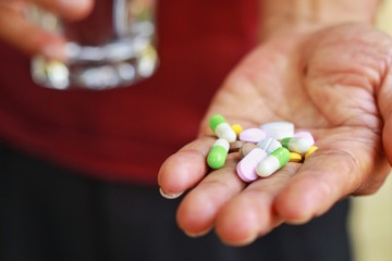 Elderly man holding pills(tablet and capsule) and glass of water in hands taking a lot of medicine, supplements or antibiotic antidepressant painkiller medication Hope for cure.Health concept.
