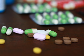 Close up at Pharmaceutical medicine pills, tablets and capsules.Blurred blister background. Heap of assorted various medicine different colors on wooden background. Health care.