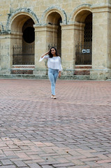 Fototapeta na wymiar Outdoor portrait of young beautiful girl 9 to 25 years old posing in street. wearing white blouse and tight jeans and sapatillas. City lifestyle. Female fashion concept.