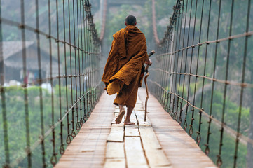 monk is walking on a wooden bridge.