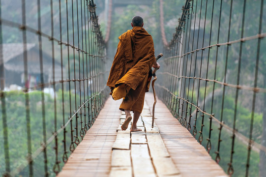 monk is walking on a wooden bridge.