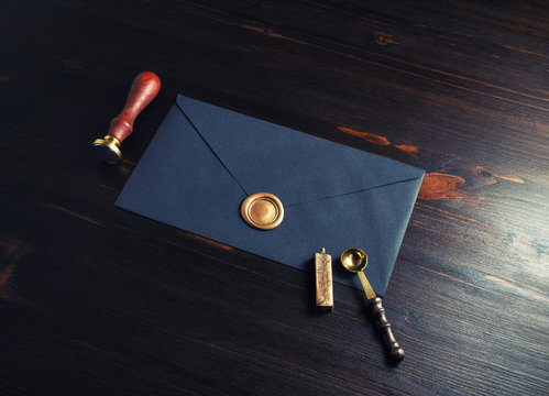 Retro postal stationery. Black envelope with golden wax seal, stamp and spoon on dark wooden background.