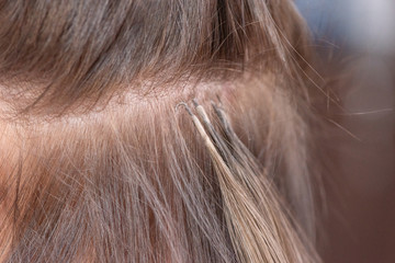 Professional process of hair extension for a woman with the help of artificial, in a beauty salon...