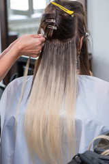 Fototapeta premium Professional process of hair extension for a woman with the help of artificial, in a beauty salon close up