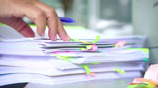 Overwork of document report and business busy Concept: Businessman manager checking and signing documents reports papers on stacks of paper files with post-it on paperwork in overload at modern office