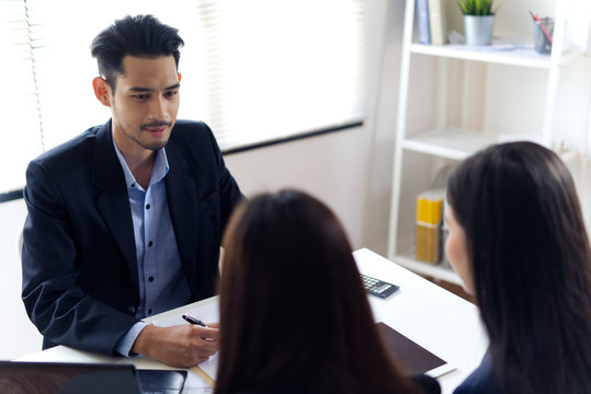 Asian manager feeling angry and blaming his two female colleagues in his office. He sitting and looking at the team with angry eyes and talking to them. Working environment concept.