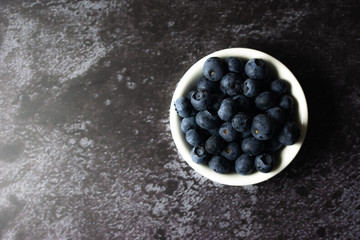 Raw blueberry in a white bowl on dark background.