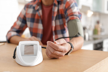 Man checking blood pressure with sphygmomanometer at table indoors, closeup. Cardiology concept