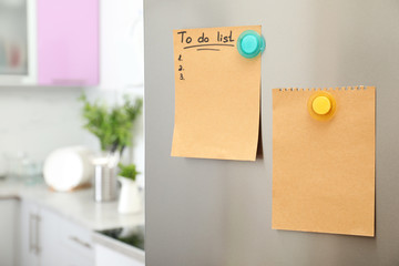 To do list and empty sheet of paper with magnets on refrigerator door in kitchen. Space for text