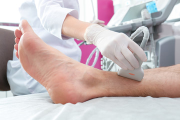 Doctor conducting ultrasound examination of patient's leg in clinic, closeup