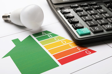 Energy efficiency rating chart, LED light bulb and calculator on white background, closeup