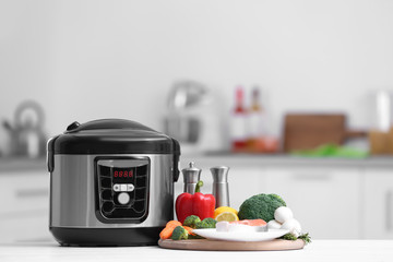 Modern multi cooker and products on table in kitchen. Space for text