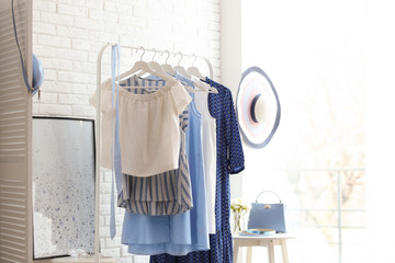 Wardrobe rack with women's clothes at white brick wall in room
