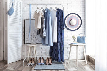 Wardrobe rack with women's clothes and different shoes at white brick wall in room