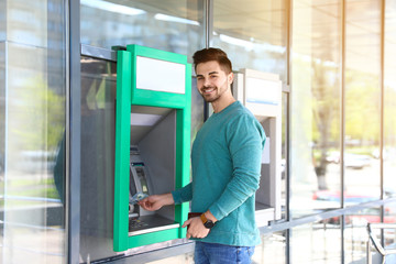 Fototapeta na wymiar Young man taking money from cash machine outdoors