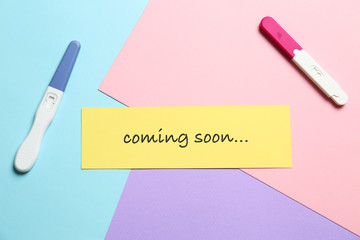 Card with words COMING SOON and pregnancy tests on color background, flat lay