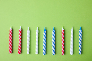 Fototapeta premium Colorful striped birthday candles on green background, flat lay