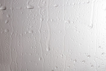 Glass with rain drops against light background