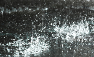 Heavy rain falling down on ground against dark background