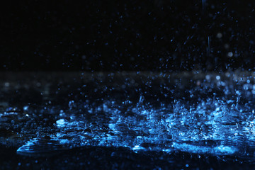 Heavy rain falling down on ground against dark background, toned in blue