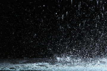 Fototapeta na wymiar Heavy rain falling down on ground against dark background