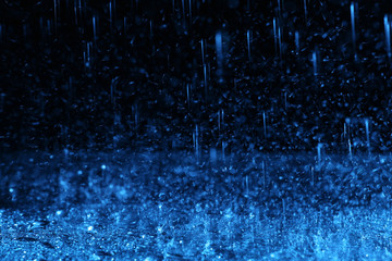 Heavy rain falling down on ground against dark background, toned in blue