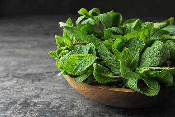 Wooden bowl full of fresh green mint on grey table, closeup. Space for text © New Africa
