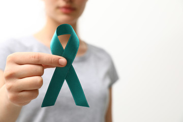 Woman holding teal awareness ribbon against light background, closeup