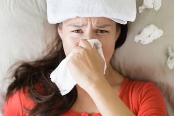 Sick woman coughing and blowing her nose, lying in bed.