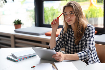 Pensive young woman studying with tablet at table in library