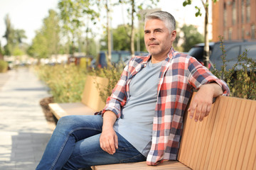 Handsome mature man on bench in park. Space for text