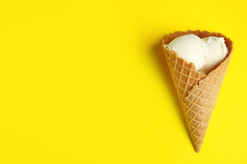 Delicious vanilla ice cream in wafer cone on yellow background, top view. Space for text