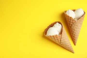 Delicious vanilla ice cream in wafer cones on yellow background, flat lay. Space for text