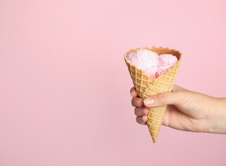 Woman holding delicious ice cream in wafer cone on pink background, closeup. Space for text