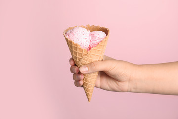 Woman holding delicious ice cream in wafer cone on pink background, closeup