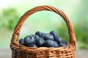 Fototapeta na wymiar Wicker basket with fresh blueberries on blurred green background, closeup