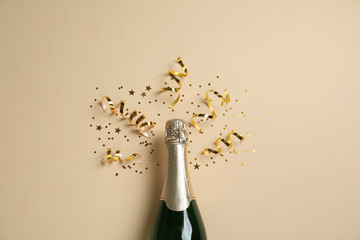 Bottle of champagne with gold glitter and confetti on beige background, flat lay. Hilarious celebration