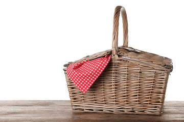 Closed wicker picnic basket with checkered tablecloth on wooden table against white background