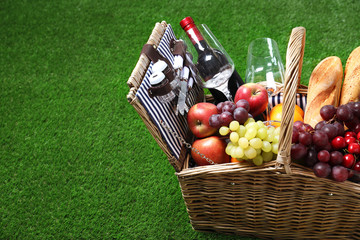 Wicker picnic basket with different products on green grass, space for text