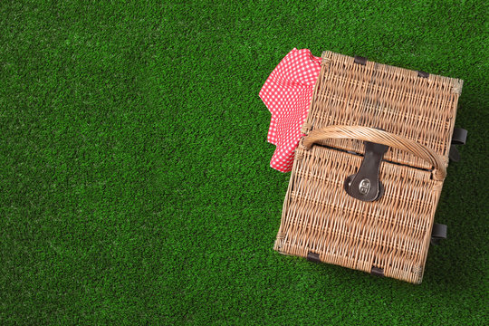 Closed wicker picnic basket on green grass, top view. Space for text