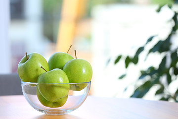 Bowl of fresh green apples on table indoors. Space for text