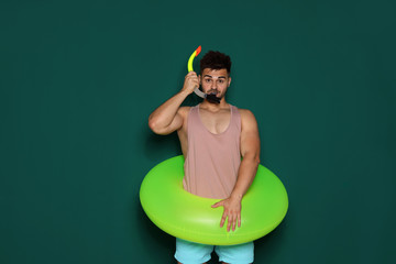 Funny young man with bright inflatable ring on dark green background